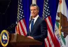 Man in suit speaking at a podium with American and California flags