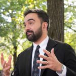 Man in a suit gesturing while speaking outdoors