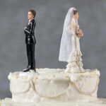 Bride and groom figurines facing away on top of a white wedding cake
