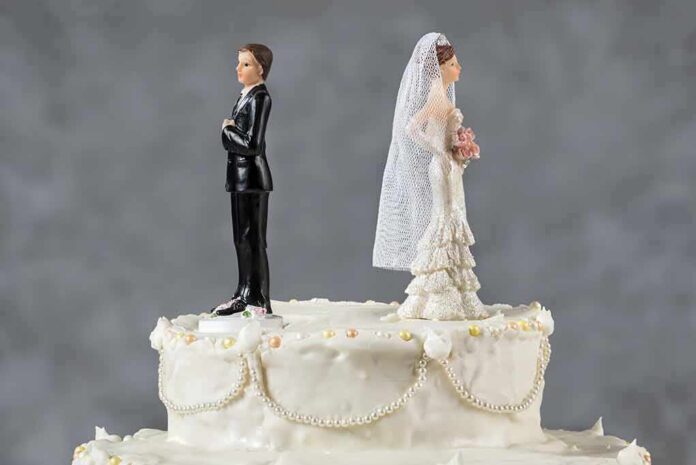 shutterstock_292107503 Bride and groom figurines facing away on top of a white wedding cake
