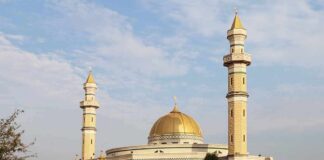 Mosque with golden dome and two tall minarets under a partly cloudy sky