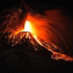 Volcano erupting at night with glowing lava and ash plume