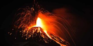 Volcano erupting at night with glowing lava and ash plume