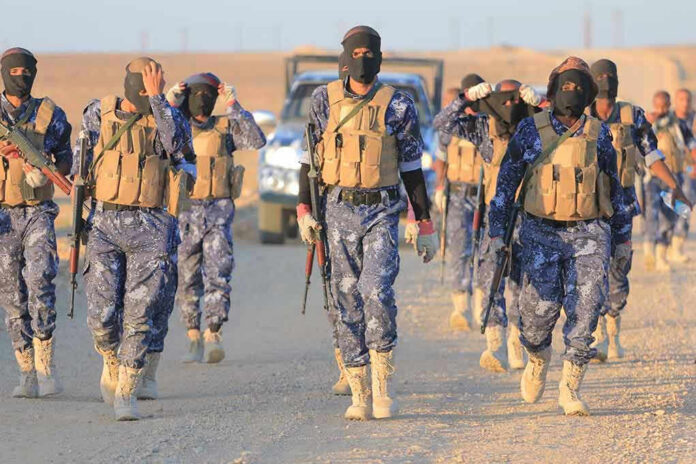 2446565389 Camouflaged soldiers wearing masks and vests walk in desert.