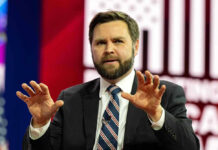 Man in suit speaking on stage with hands raised