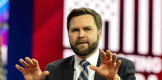 Vance Slams ‘Dishonest’ Media Perks Man in suit speaking on stage with hands raised
