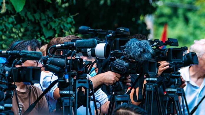 TV news cameras crowding together at an outdoor event