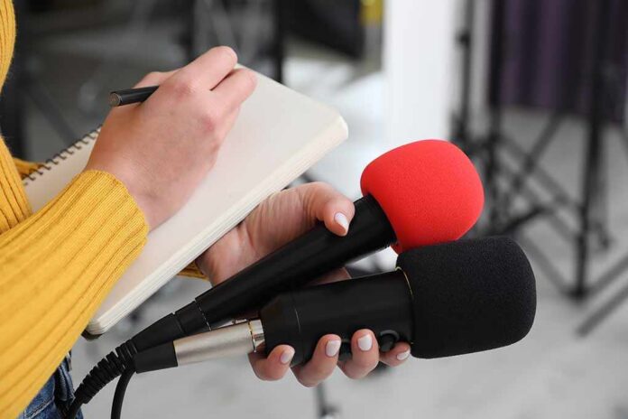 Professional,Journalist,With,Microphones,Taking,Notes,Indoors,,Closeup Journalist holding two microphones while writing in a notebook