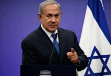 man in suit speaking at a podium with an Israeli flag