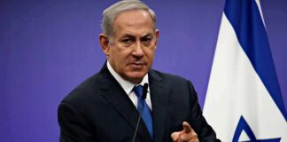 Diplomats Bolt As Netanyahu Doubles Down man in suit speaking at a podium with an Israeli flag