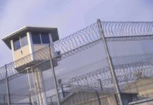 Judge Freezes ICE Build Over Toxic Fears Prison watchtower behind barbed wire fencing