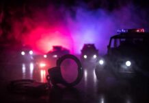 Illegal Guns Turn Night Out Into Warzone Handcuffs on a surface with police cars and flashing lights in the background