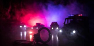 Illegal Guns Turn Night Out Into Warzone Handcuffs on a surface with police cars and flashing lights in the background