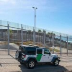 Border patrol SUV parked by tall metal fence near the coast