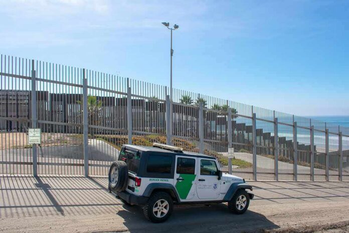 Border patrol SUV parked by tall metal fence near the coast