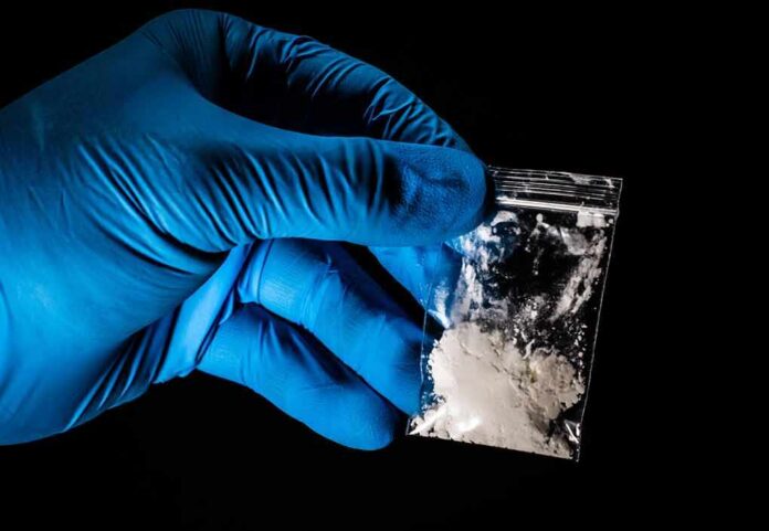 shutterstock_1272023845 Gloved hand holding a small plastic bag of white powder
