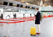 Mystery Trade-Off Brings American Home Traveler wearing a mask stands by yellow suitcase at empty airport check-in