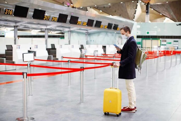 Traveler wearing a mask stands by yellow suitcase at empty airport check-in