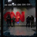 police officers inside lobby seen through shattered glass window