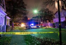 Teen Party Erupts In Gunfire Police car blocks residential street at night behind caution tape
