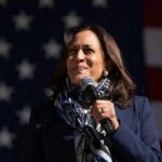 Kamala Harris speaking into a microphone in front of a U.S. flag backdrop