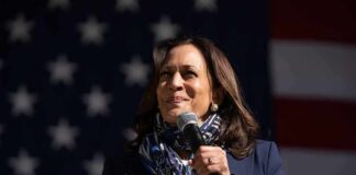 Kamala Harris speaking into a microphone in front of a U.S. flag backdrop