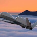 military drone flying above clouds at sunset