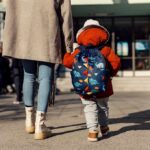 Child with backpack walking to school with adult