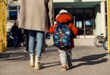 Child with backpack walking to school with adult