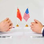 Two diplomats sit across table with China and United States flags between them