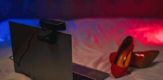 AI Porn Kingpins Get Domain-Ripped Laptop with webcam on a bed beside red high heels