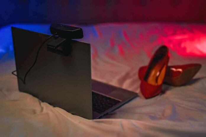 shutterstock_2200761975 Laptop with webcam on a bed beside red high heels