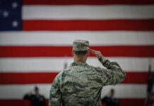 Hegseth Declares War On Pentagon Bureaucracy Soldier saluting before a large American flag