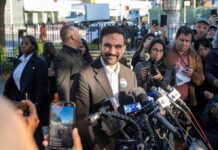 Zohran Mamdani speaks at a press conference; Julia Bacha is visible among the crowd