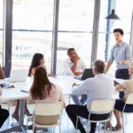 Team meeting with a man standing and speaking to colleagues around a table