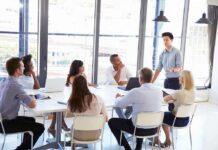 Pay Protections Promised – Or Loophole? Team meeting with a man standing and speaking to colleagues around a table