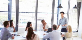 Team meeting with a man standing and speaking to colleagues around a table