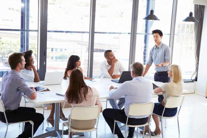 Team meeting with a man standing and speaking to colleagues around a table