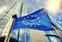 EU – Canada Gambit Triggers Tariff Warning European Union flag waving in front of modern glass office buildings