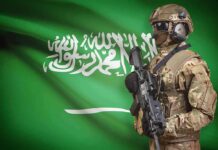 Nuclear Wildcard Locks Arms With Riyadh Soldier in tactical gear stands before a green flag
