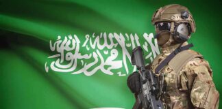 Nuclear Wildcard Locks Arms With Riyadh Soldier in tactical gear stands before a green flag