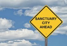 Sanctuary Clash Sparks Capitol Firestorm yellow road sign with sanctuary city message against cloudy sky