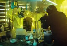 Emergency Powers Fly—Residents Gasp For Air armed officer confronts people in hazmat suits inside a lab