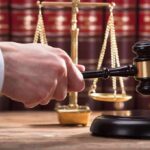 Judge's hand holding gavel near scales of justice