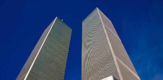Twin rectangular skyscrapers rising above a hotel facade against a clear blue sky