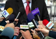 TV Giants Accused Of Illegal Boycott Press microphones surround a suited spokesperson