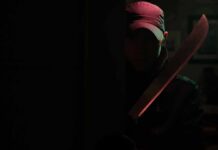Person in cap holding a large machete in dark doorway