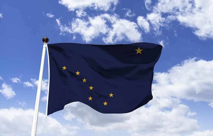 shutterstock_1363238492 Alaska state flag waving on a pole against a blue sky