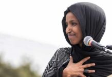 Omar Answers Questions After Federal Home Search Ilhan Omar speaking at a microphone with hand on chest
