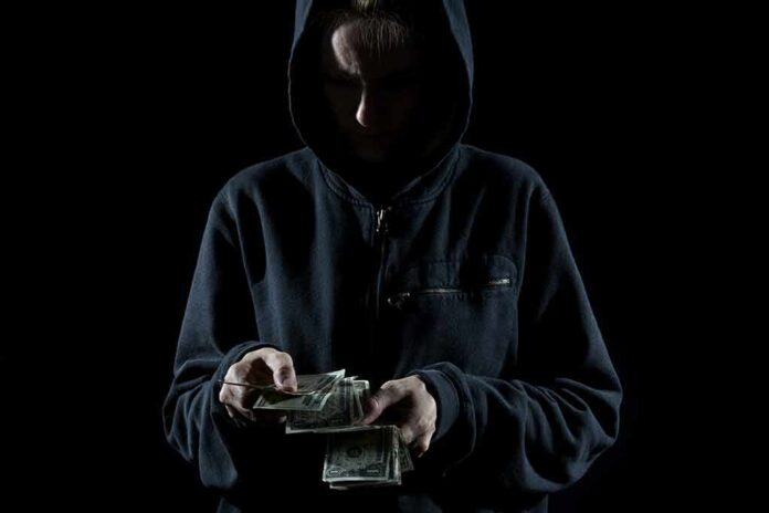shutterstock_161246150 Person in a hoodie counting cash in low light